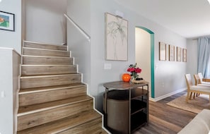 Un escalier avec des marches en bois, une petite table sur laquelle se trouve un vase et un objet sphérique, et un coin repas avec des chaises et une table.