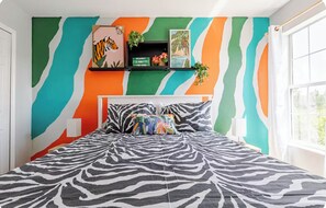 A bedroom with a zebra-patterned bedspread, a tiger-themed picture frame, and a wall with a wavy color pattern.