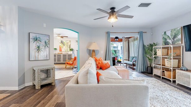 A living room with a sofa, a ceiling fan, a lamp, and a bookshelf. - Family Paradise: 5BR Kissimmee Home with Private Pool and Pet Friendly (Kissimmee)