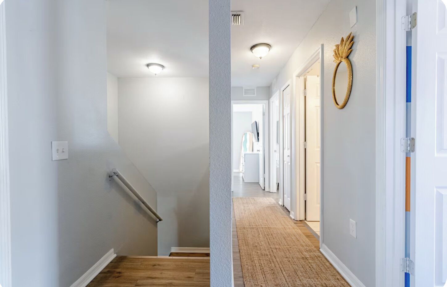 A hallway with a wooden staircase, a textured carpet, and a decorative wall piece.