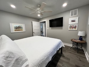 A bedroom with a bed, a ceiling fan, a TV, and framed pictures on the wall.