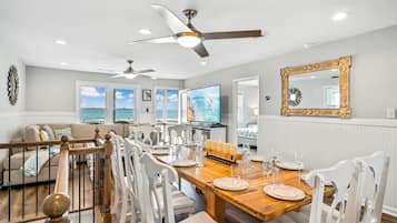 A dining area with a wooden table set for six, white chairs, and a ceiling fan.
