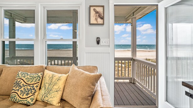 Habitación frente a la playa con un sofá color beige, una obra de arte enmarcada y vista al océano a través de amplias ventanas.