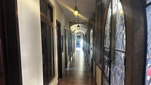 A long, narrow hallway with tiled flooring, large windows with decorative frames, and a ceiling light fixture. - Don Valentino (Antigua Guatemala)