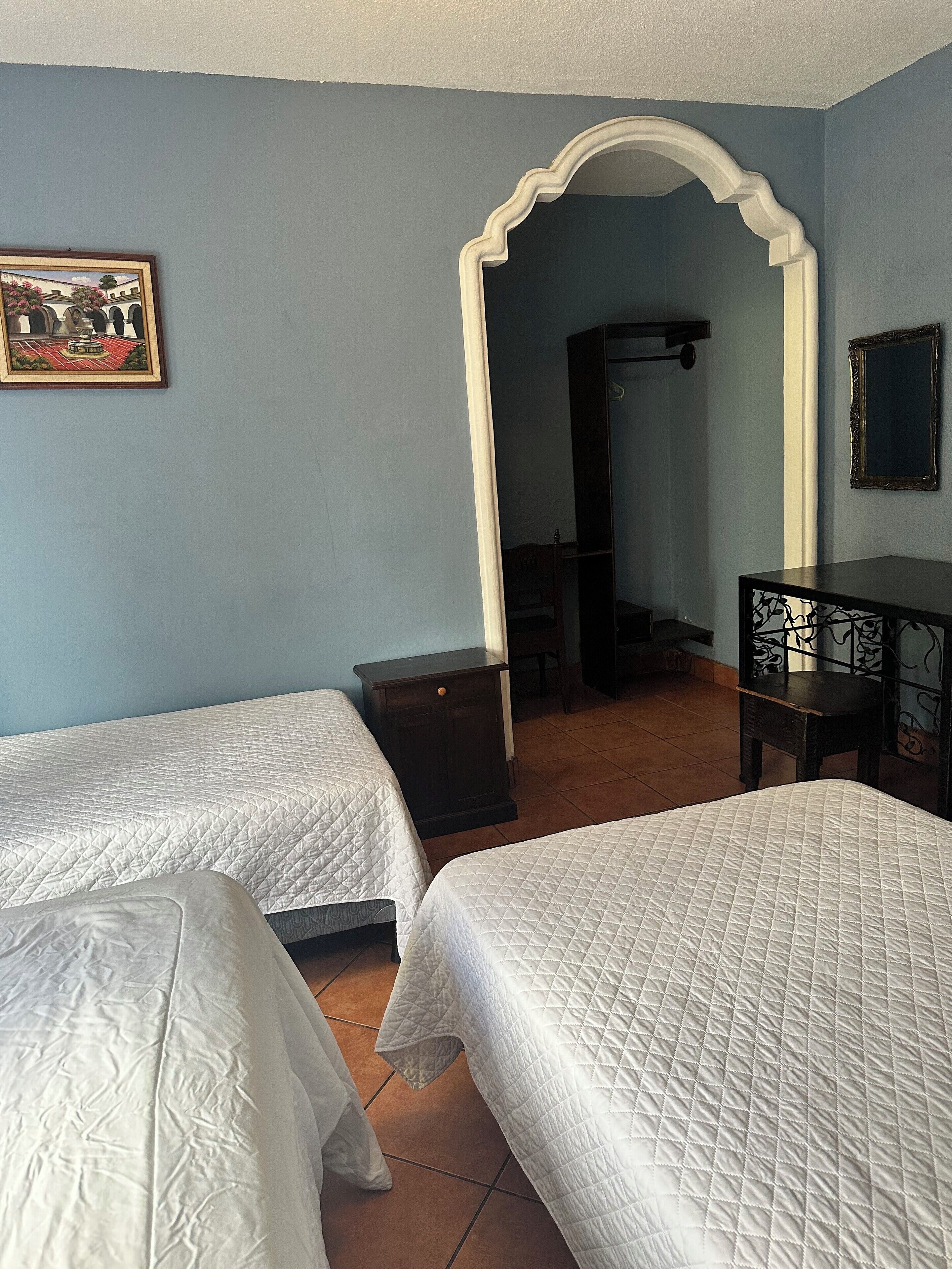 Una habitación con dos camas, un armario de madera, un espejo y un cuadro en la pared.