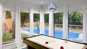 A pool table in a room with large windows overlooking a swimming pool, white curtains, and a disco ball. - Waterfront / Beauty Bar / Family Fun / 2 King Beds (Granbury)