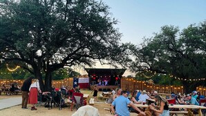 An outdoor event with wooden picnic tables and a stage for performances. - Waterfront / Beauty Bar / Family Fun / 2 King Beds (Granbury)