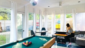 A pool table with a PONG sign, a disco ball, and a view of a backyard with a wooden fence and outdoor seating. - Waterfront / Beauty Bar / Family Fun / 2 King Beds (Granbury)