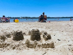 Una playa arenosa con castillos de arena y gente al fondo.