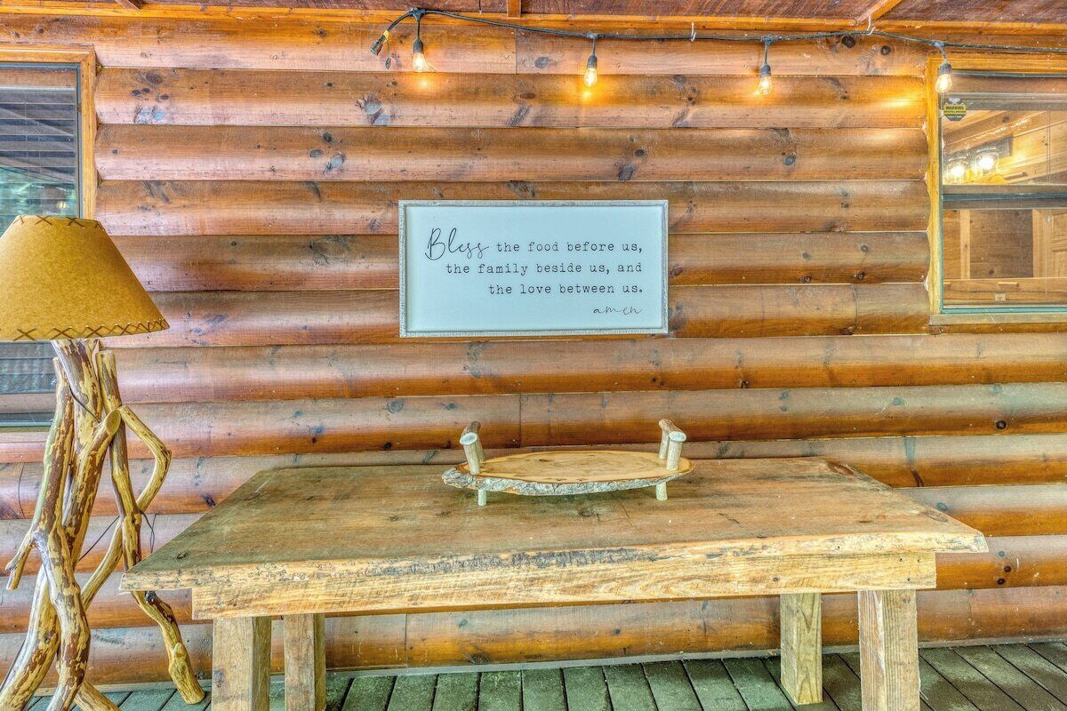 Ein rustikales Holzhaus-Interieur mit einem Holztisch, einer Lampe und einem gerahmten Zitat an der Wand.