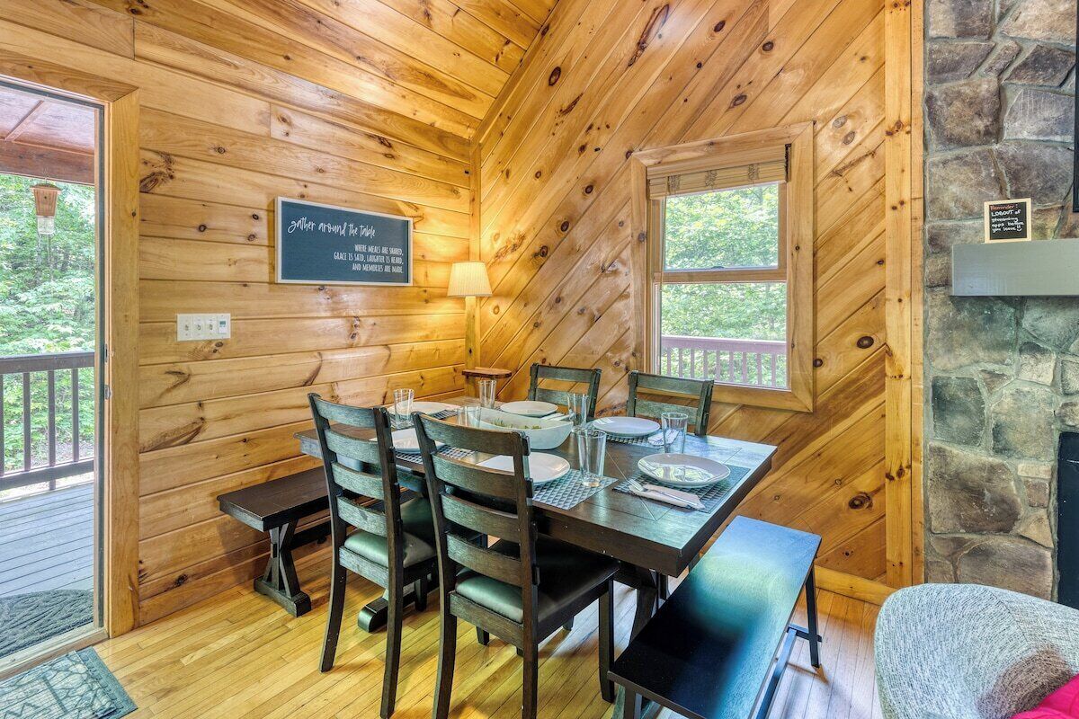 A wooden cabin with a dining area featuring a table set for four, wooden walls, and a stone fireplace.