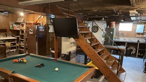 Une table de billard avec des billes, un téléviseur fixé au mur et un escalier en bois.