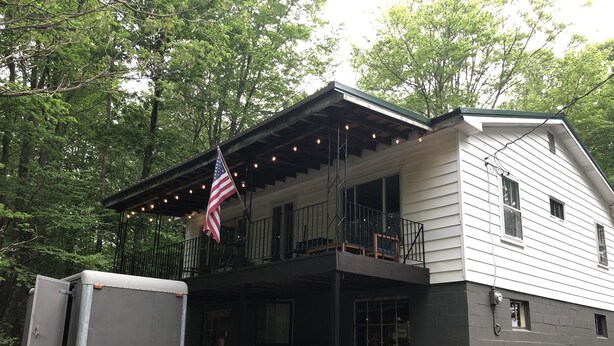 Une maison à deux étages avec un balcon, un drapeau américain et une remorque garée devant.