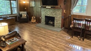 Un salon chaleureux avec une cheminée, des murs en bois, un téléviseur et un coin repas comprenant des chaises et une table.