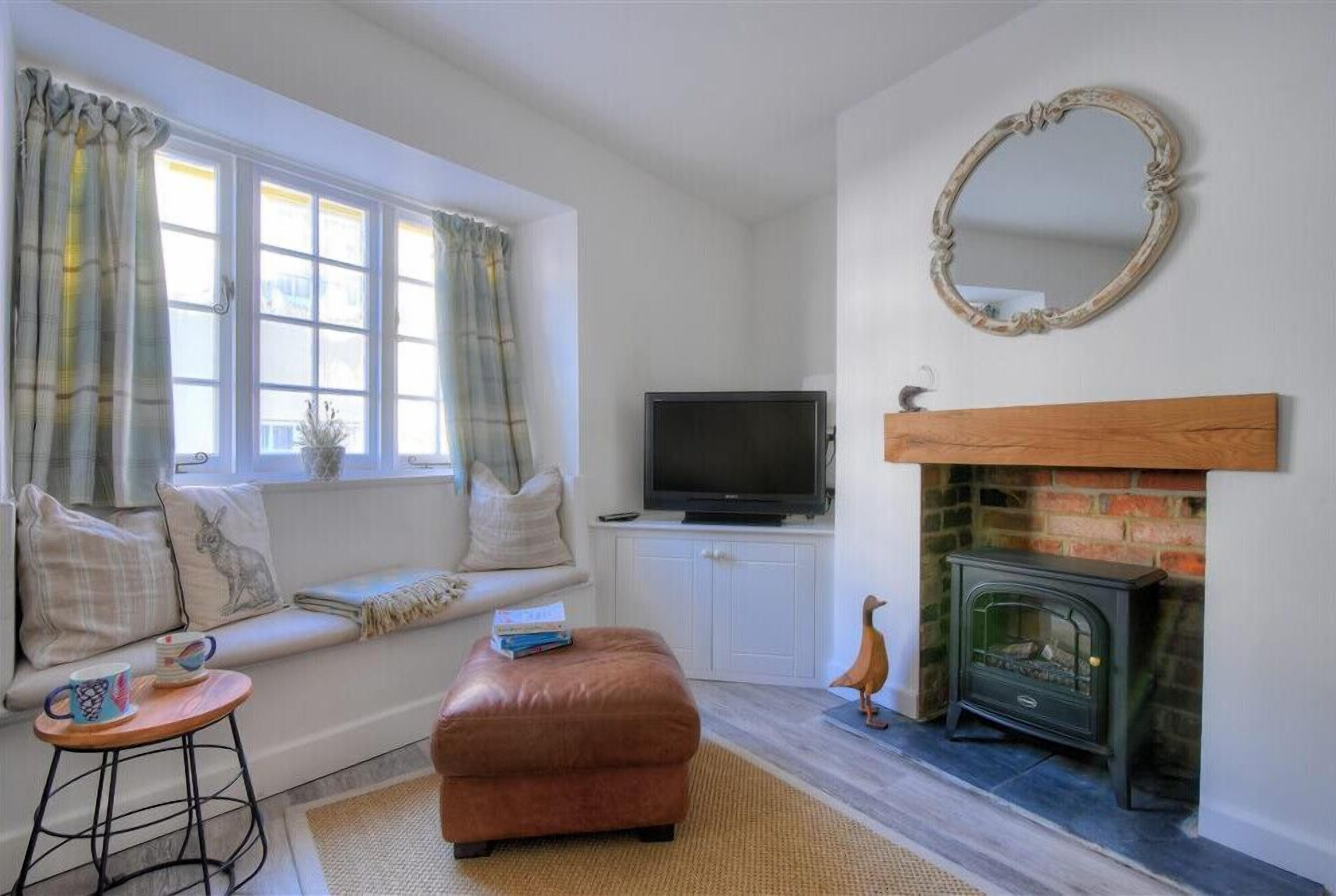 A cozy living room with a fireplace, a television on a white cabinet, a sofa with cushions, and a small wooden table with a mug.
