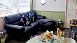 Una sala de estar con un sofá de cuero negro, una mesa redonda de comedor con platos, vasos y una vela.