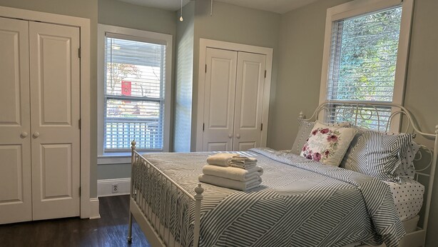 Un dormitorio con una cama, dos ventanas, un ventilador de techo y una puerta.