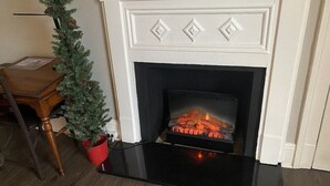 Una chimenea con hogar negro, repisa blanca y detalles decorativos, además de una pequeña planta en maceta a un lado.