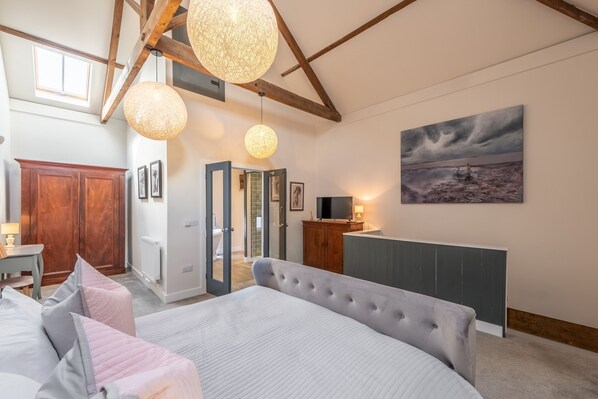 A bedroom with a large bed, wooden ceiling beams, and a painting of a stormy sea on the wall.
