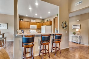 A kitchen with wooden cabinets, a white refrigerator, and a bar area with three stools.
