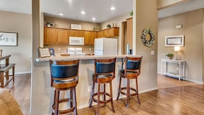 A modern kitchen with wooden cabinets, a central island with bar stools, and a dining area with a bench. - Golf Lover's Paradise with Onsite Course, Games & $400 Daily Tickets Near Silver Dollar City (Reeds Spring)