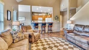 A spacious living room with leather sofas, a checkered rug, and a kitchen in the background. - Golf Lover's Paradise with Onsite Course, Games & $400 Daily Tickets Near Silver Dollar City (Reeds Spring)