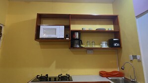 Een kleine keuken met een witte magnetron, een koffiezetapparaat en een gasfornuis.