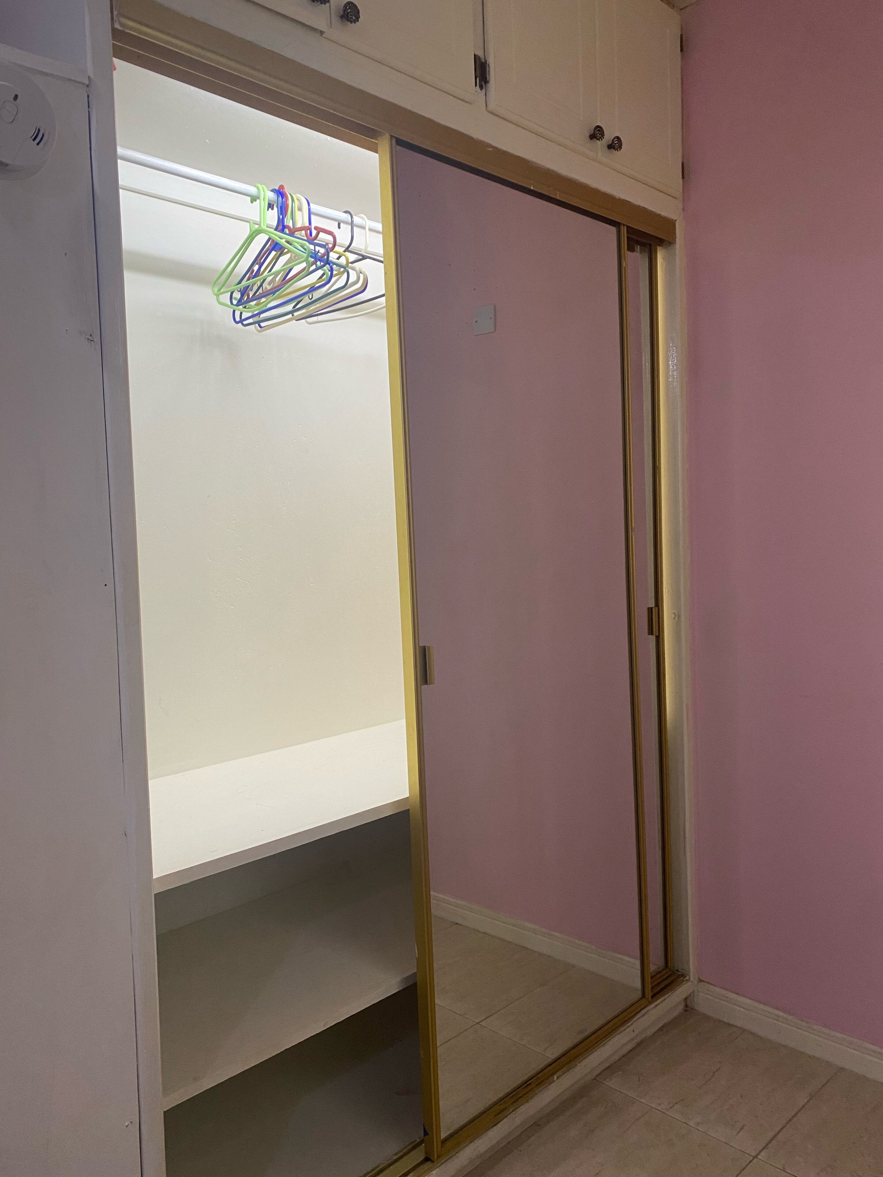 A room with a sliding door closet, a whiteboard, and a clothes rack with colorful items.