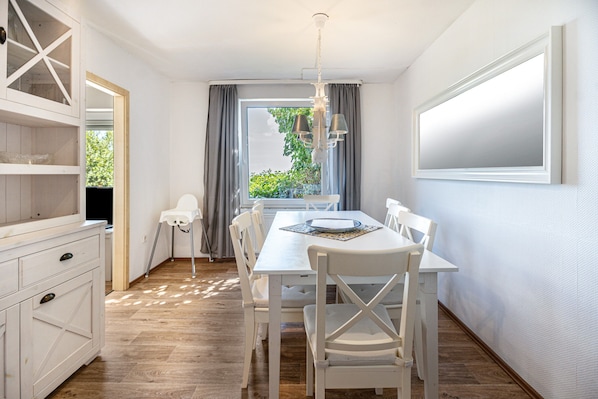 Una cocina moderna con armarios blancos, una mesa de comedor con sillas y un amplio ventanal con cortinas.