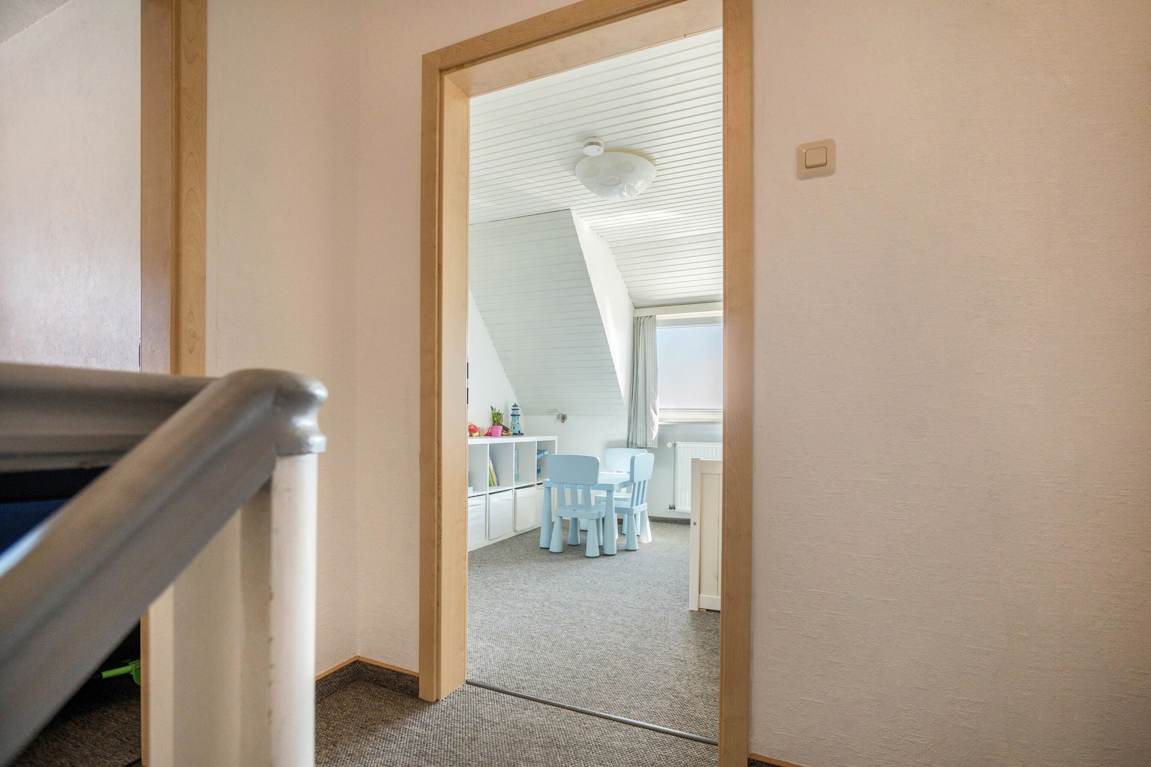 Ein Zimmer mit schrägen Wänden, einem Essbereich mit Stühlen und Tisch sowie einem sichtbaren Heizkörper.
