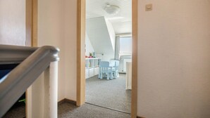 Una habitación con techo inclinado, una zona de comedor con sillas y una mesa, y un radiador a la vista.