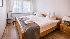 Una cama de madera con almohadas, una mesita de noche, una silla y una ventana con cortinas.