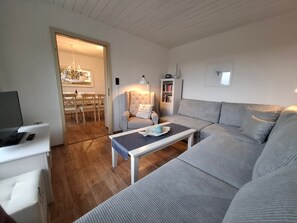 Un salon comprenant un canapé, une table basse, un fauteuil, un téléviseur et une bibliothèque.