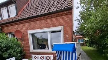 Ein Backsteinhaus mit Ziegeldach, einem weißen Fenster und einer Terrasse mit Tisch und Stühlen.