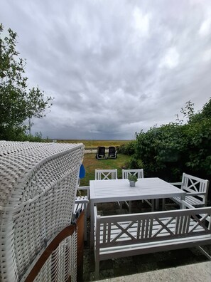 Eine Terrasse mit einem weißen gewebten Tisch und Stühlen, Blick zum Himmel und einem Rasen.