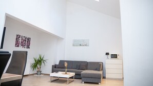 Una sala moderna con un sofá gris, una mesita de centro, una planta en maceta y un armario blanco.
