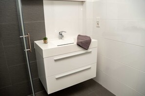 Ein Badezimmer mit weißem Waschtisch, einem kleinen Topfpflanzen, einem Handtuch und einer Glasdusche.