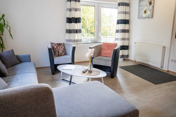 Ein modernes Wohnzimmer mit einer Couch, einem Sessel, einem Couchtisch, einer Heizung und einem Fenster mit Vorhängen.