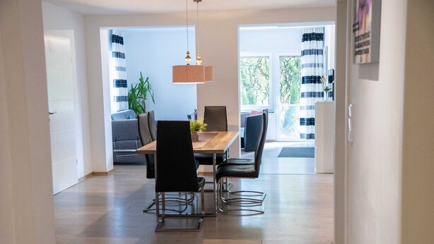 A dining area with a wooden table, four chairs, a hanging light fixture, and a view through a glass door. - 'Villa Nordhang - Apartment 4' with Mountain View, Balcony & Wi-Fi (Winterberg)
