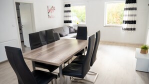 A modern dining area with a wooden table and black chairs, a grey sofa, and a view of the outdoors through a window.