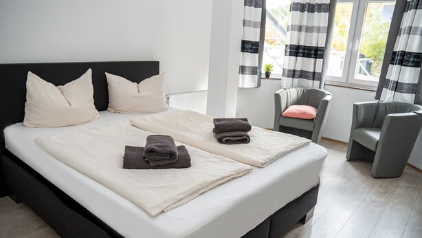 A modern hotel room with a large bed, two pillows, a chair, and a view of the outdoors.
