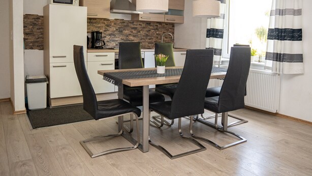 Une cuisine moderne équipée d’un four à micro-ondes, d’une cuisinière et d’un évier. On y trouve une table à manger avec des chaises et une petite plante en pot. La pièce est dotée d’une fenêtre avec des rideaux et offre une vue sur l’extérieur.