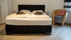 Un lit double avec deux oreillers, une chaise avec un coussin et une lampe sur une table de chevet.