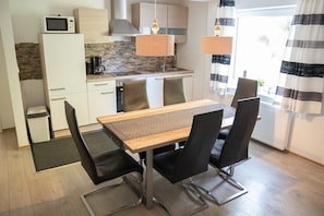 A modern kitchen with white cabinets, a microwave, and a coffee maker. There is a dining table with four chairs and a rug leading to the door.