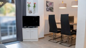 Un espace repas moderne comprenant un téléviseur à écran plat, deux chaises noires, un meuble blanc et une petite table.