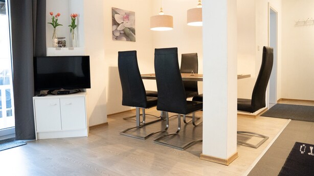 Un espace repas moderne avec un téléviseur, des chaises noires et un meuble blanc.