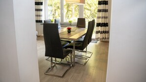 A dining area with a wooden table, four chairs, a hanging light fixture, and a view of trees through large windows. - 'Villa Nordhang - Apartment 7' with Mountain View, Balcony & Wi-Fi (Winterberg)