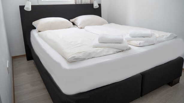A neatly made bed with white linens and towels, a dark headboard, and a window with curtains. - 'Villa Nordhang - Apartment 7' with Mountain View, Balcony & Wi-Fi (Winterberg)