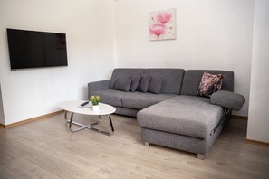 En moderne stue med en grå hjørnesofa, et lille hvidt sofabord og et fladskærms-tv monteret på væggen.
