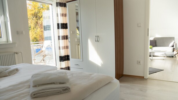 A hotel room with a bed, a wardrobe, a door leading to a balcony, and a seating area with a sofa and table. - 'Villa Nordhang - Apartment 8' with Mountain View, Balcony & Wi-Fi (Winterberg)